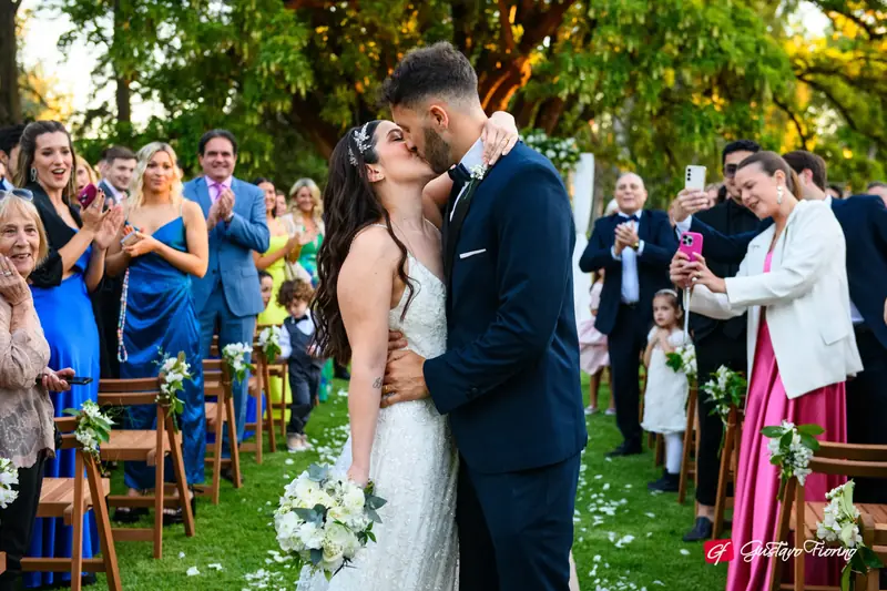 Novios besándose en el pasillo de la ceremonia con los invitados alrededor