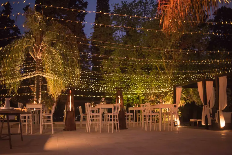 Mesas bajo guirnaldas de luces entre los árboles de noche